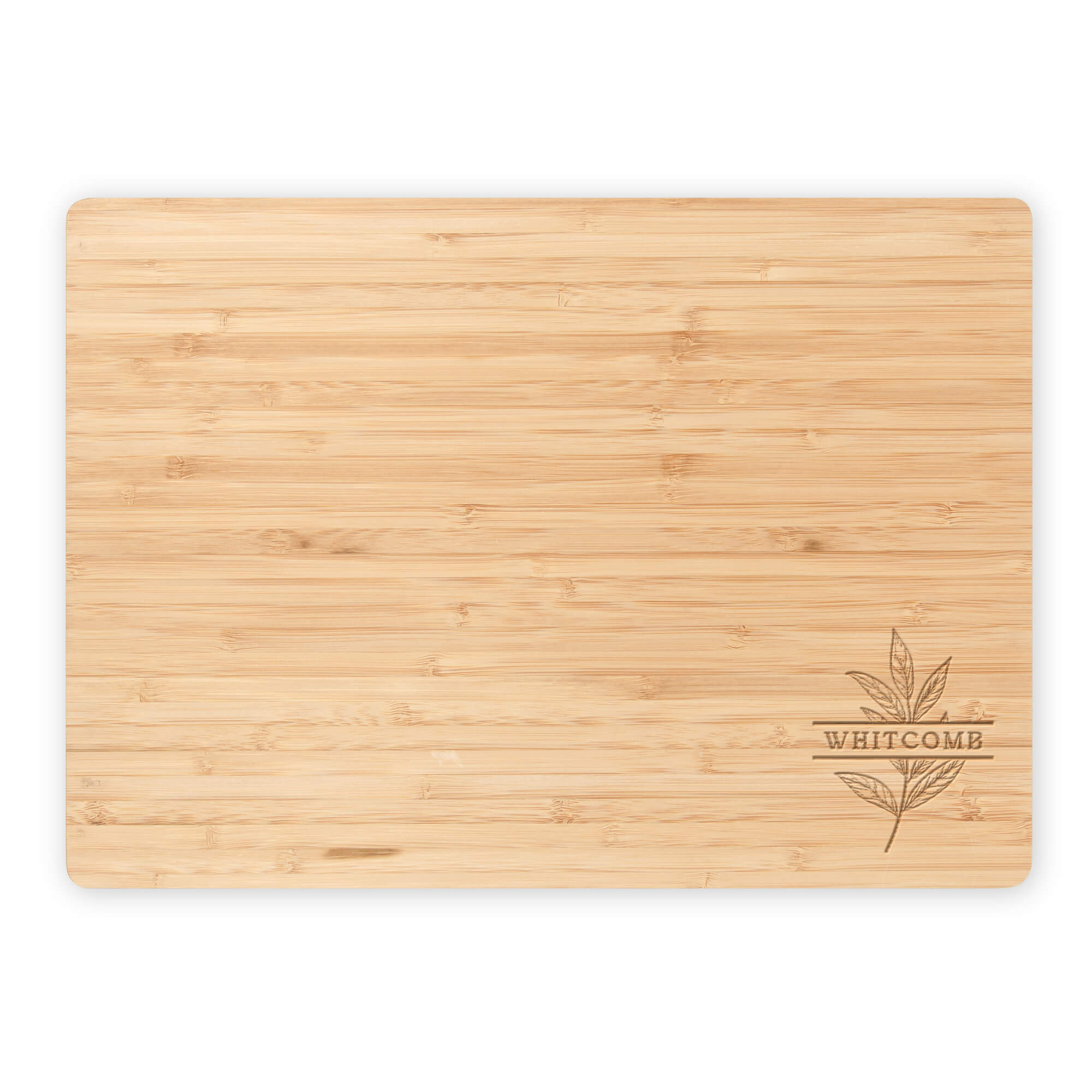Flat lay of personalized bamboo cutting board featuring “Whitcomb” and a botanical leaf engraving on a clean white background.