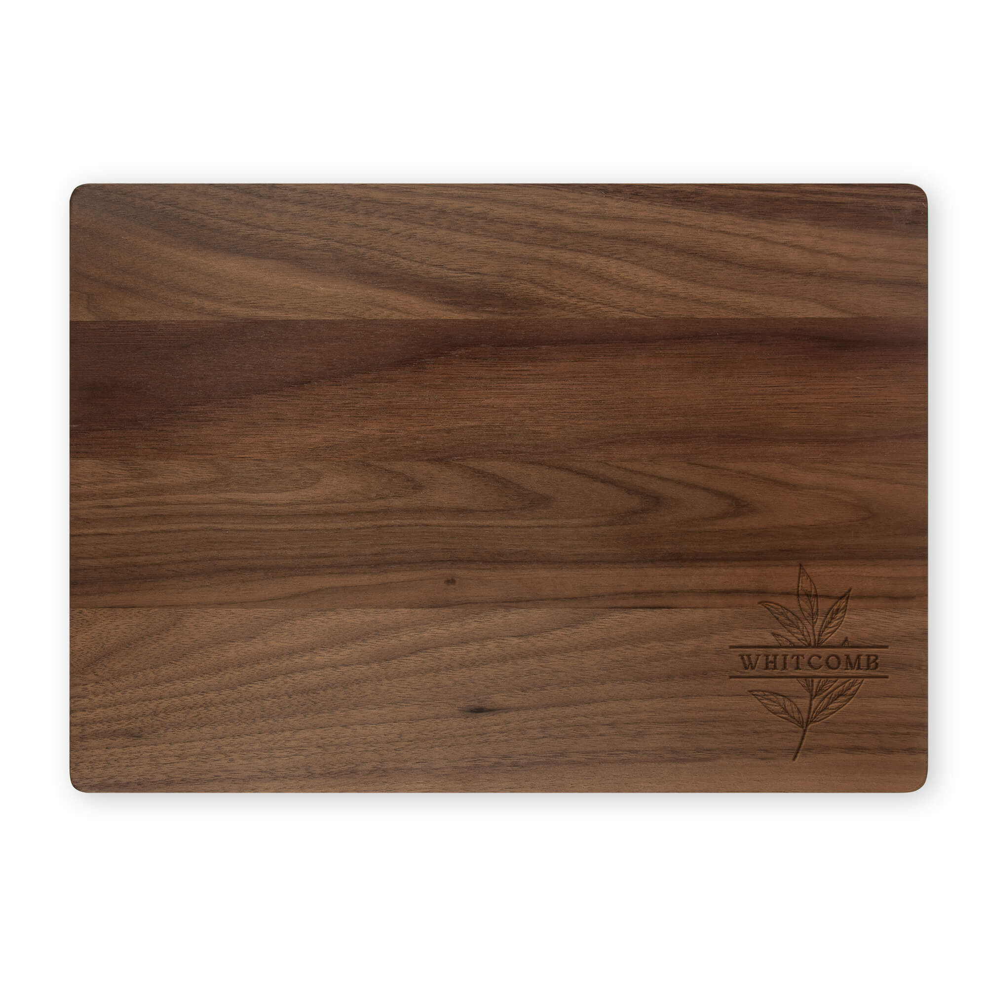 Flat lay of personalized walnut cutting board with “Whitcomb” and a botanical leaf engraving on a white background.