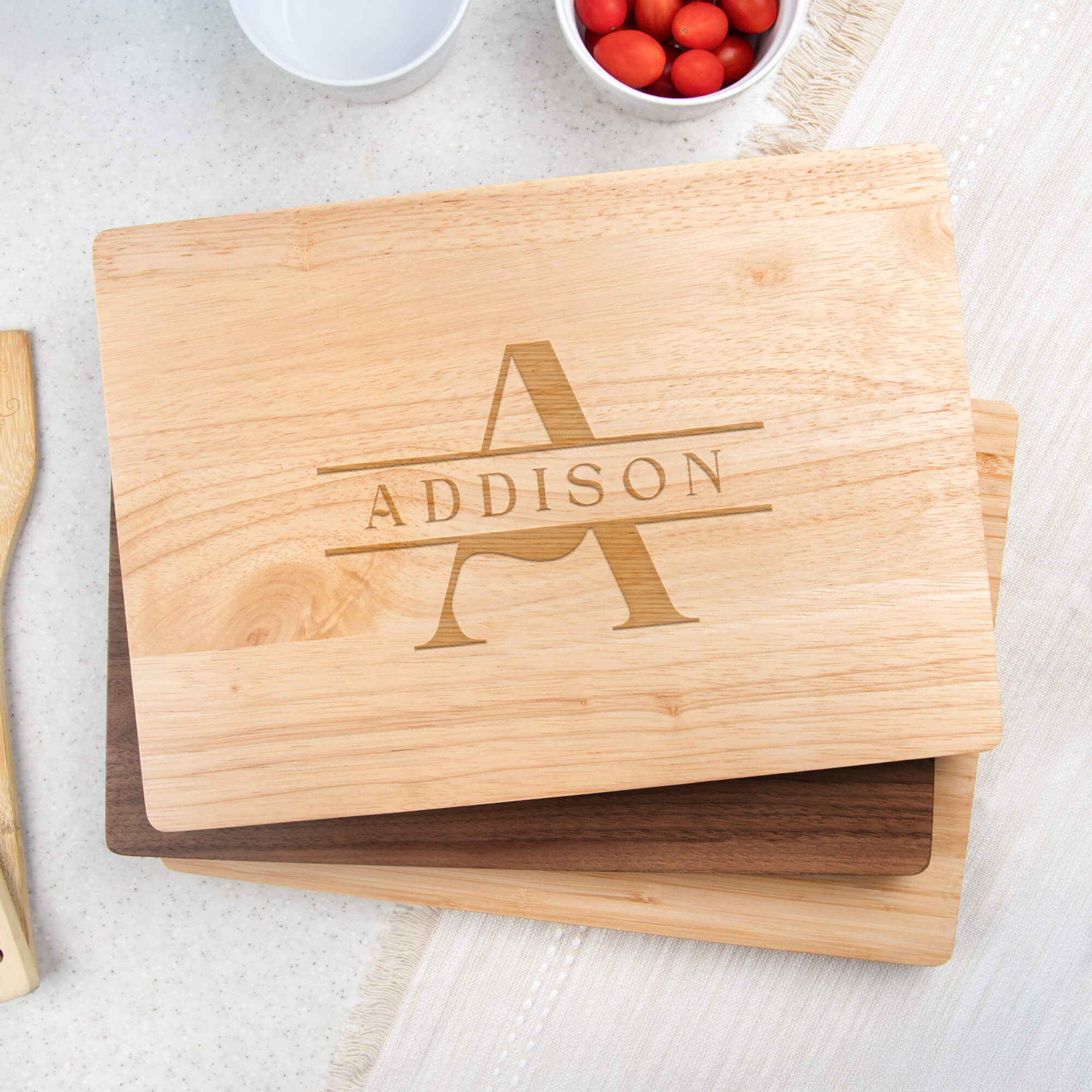 Maple cutting board with classic A and ADDISON monogram stacked on walnut and bamboo boards