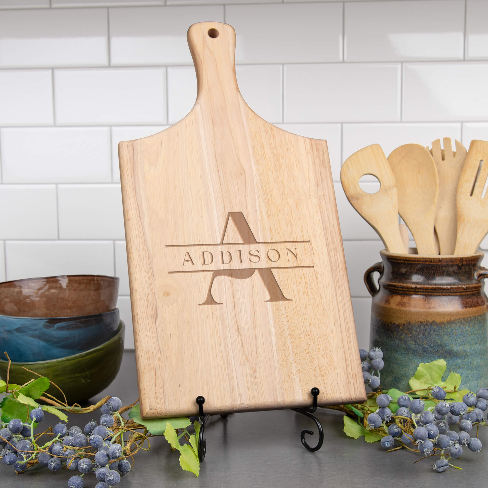 Maple paddle cutting board with classic A and ADDISON monogram displayed on a stand in a kitchen setting