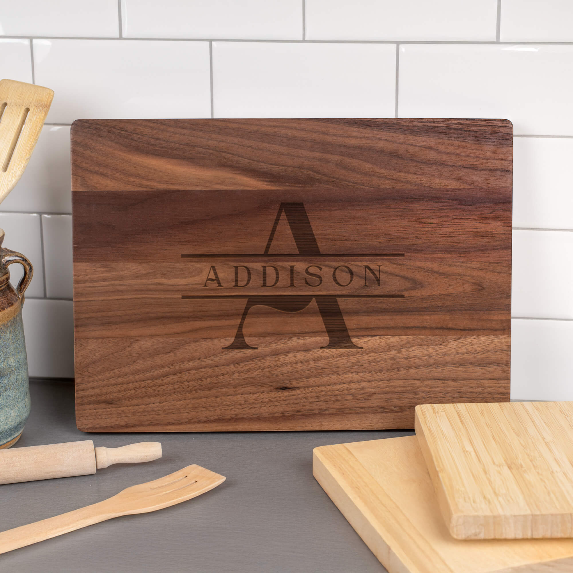 Personalized walnut cutting board engraved with large A and ADDISON name in a kitchen setting