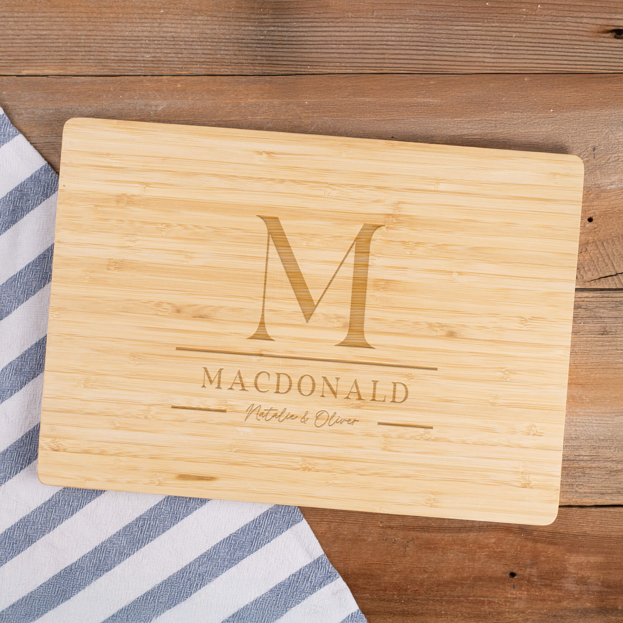 Bamboo cutting board engraved with M monogram, MacDonald family name, and script names Natalie & Oliver on rustic wooden surface