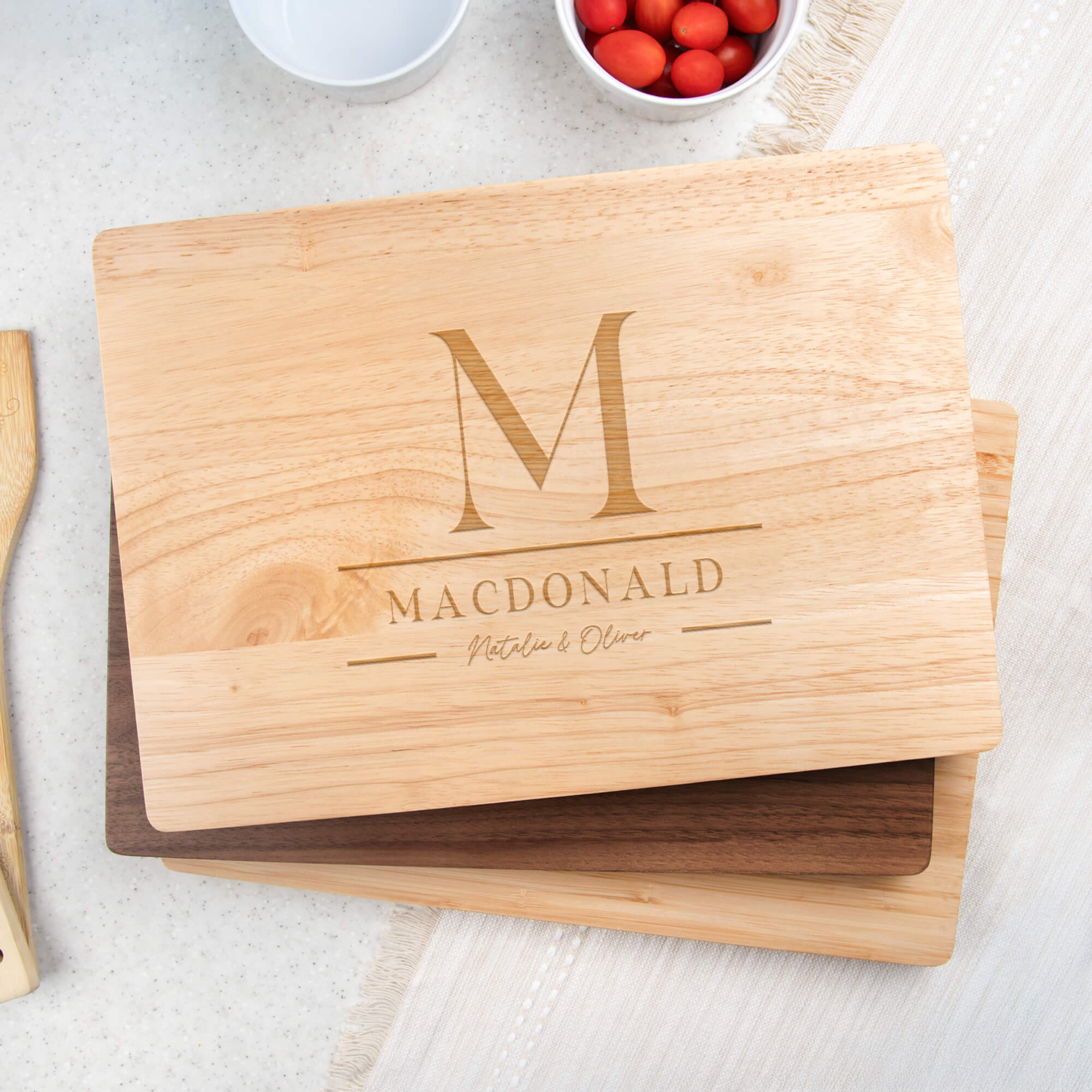 Maple paddle cutting board with stacked M monogram, MacDonald family name, and script Natalie & Oliver displayed on a stand in a kitchen