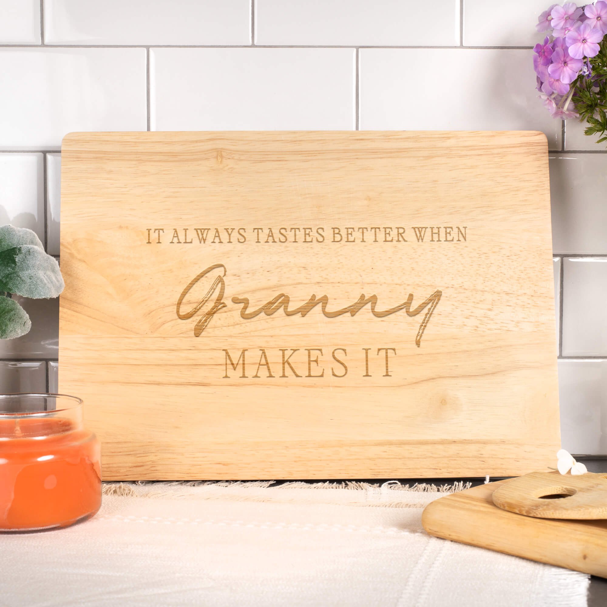 Engraved maple cutting board with “It Always Tastes Better When Granny Makes It,” styled with flowers and candles. Heartfelt kitchen or holiday gift for Grandma.