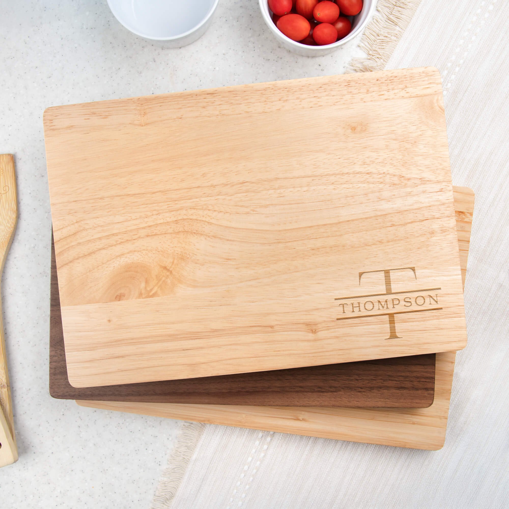 Engraved Family Name Thompson Monogram Cutting Board in Maple Wood on a table cloth next to a bowl of tomatoes