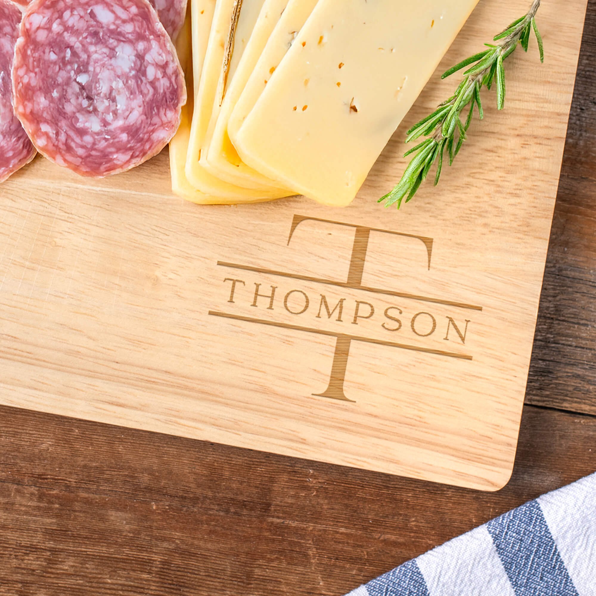 Engraved Family Name Thompson Monogram Cutting Board in Maple Wood next to assortment of charcuterie foods