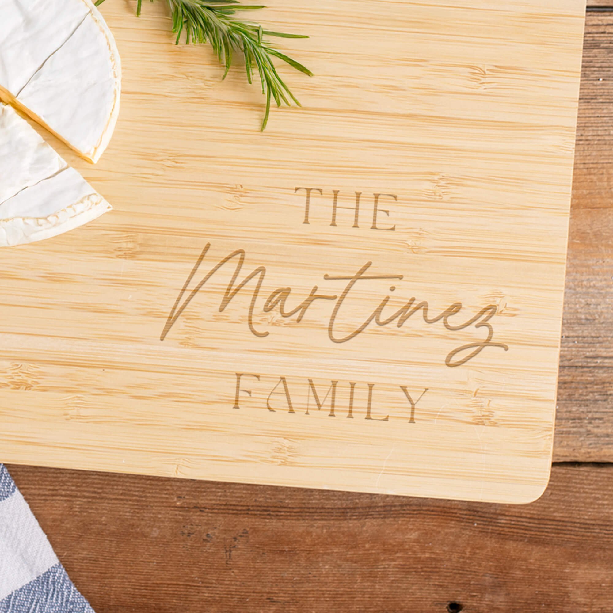 Custom Family Script Engraved Bamboo Cutting Board zoomed in to highlight the design, next to brie cheese and rosemary