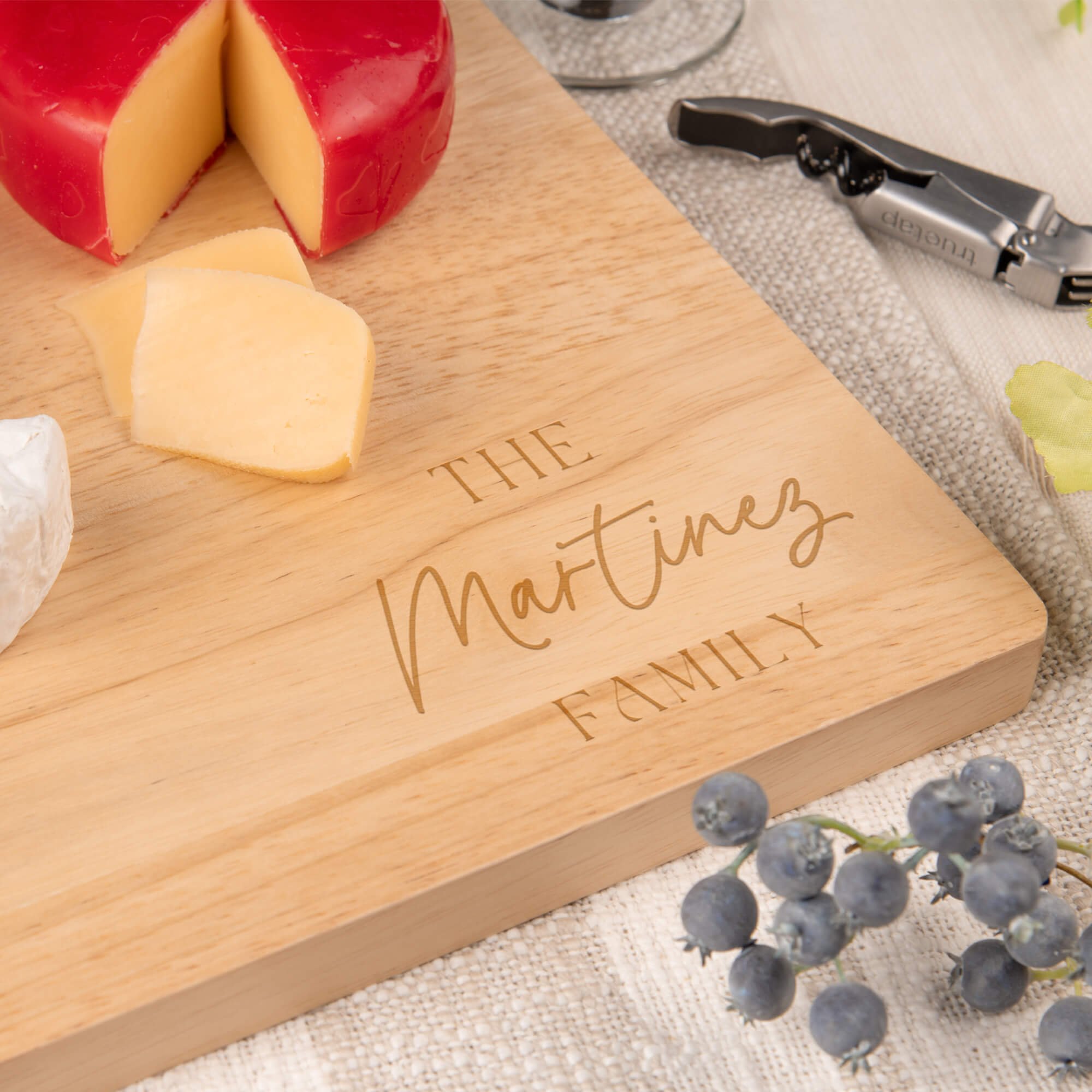 Close-up of personalized maple cutting board engraved with “The Martinez Family,” styled with cheese, grapes, and a corkscrew for an elegant kitchen setting.