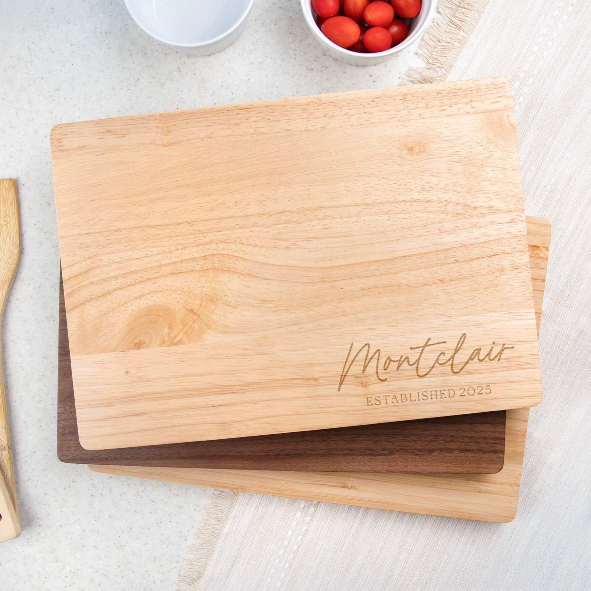 Maple cutting board engraved with “Montclair Established 2025” stacked with walnut and bamboo boards. Custom engraved cutting board or anniversary gift for home kitchens.