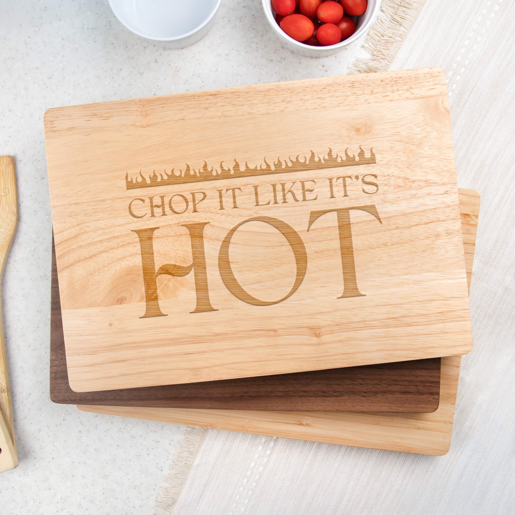Funny engraved maple cutting board with the phrase “Chop It Like It’s Hot,” styled with bowls of tomatoes and kitchen utensils. Perfect gift for home cooks and BBQ lovers.
